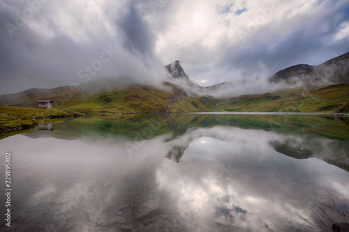 Esel-summit in mystic clouds and vivid green rolling hills reflected in Bachalpsee Switzerland