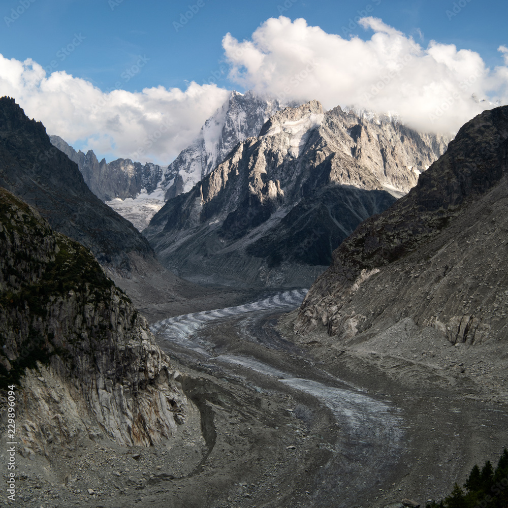 Meandering galcier Mer de Glace Chamonix and Aguille du Tacul with cloud layer and blue sky