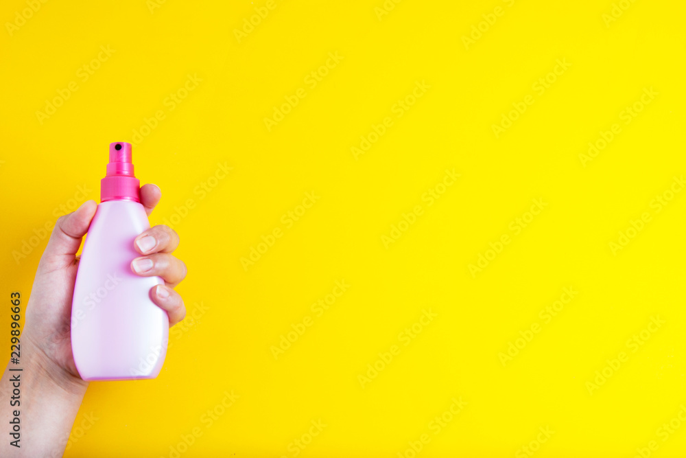 Hand holding pink spray cosmetic plastic bottle, isolated on yellow background with copy space. Hand holding pink spray cosmetic plastic bottle, isolated on yellow background with copy space.