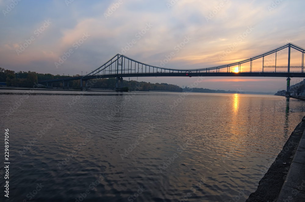 Obraz premium Sceniczny jesień krajobraz rzeka Dnipro i most dla pieszych. Słońce odbija się w wodzie. Selektywna ostrość z obiektywem szerokokątnym. Kijów, Ukraina