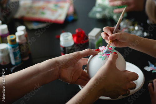 Mother and daughter are making a DIY Christmas tree ball at the table 