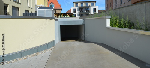 Moderne Tiefgaragen-Zufahrt mit Automatik-Tor. Einfahrt mit Beton-W  nden und Metall-Verblendung