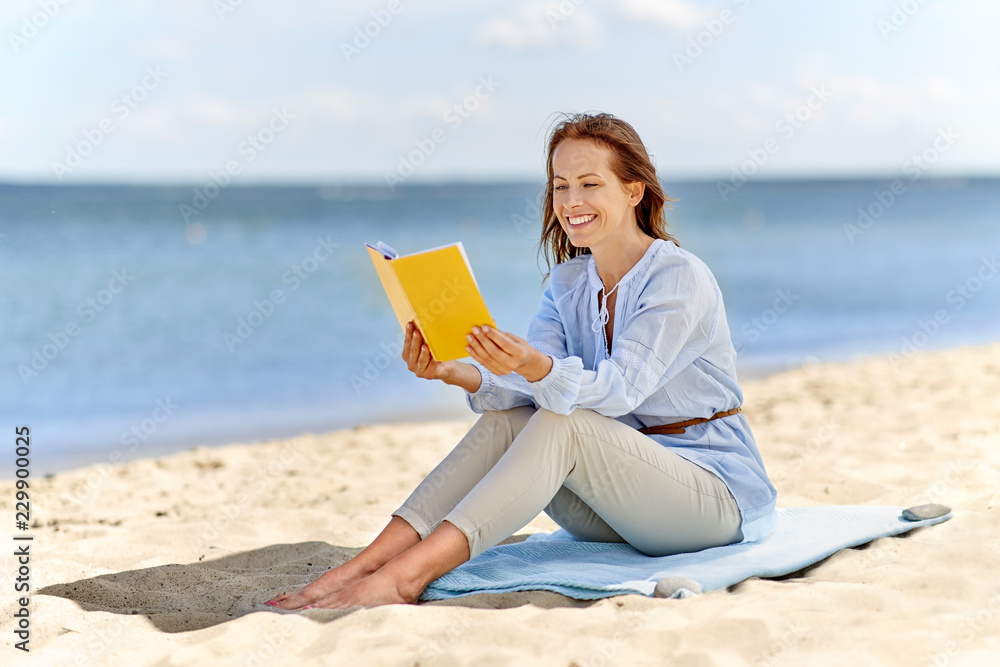 people and leisure concept - happy smiling woman reading book on summer beach