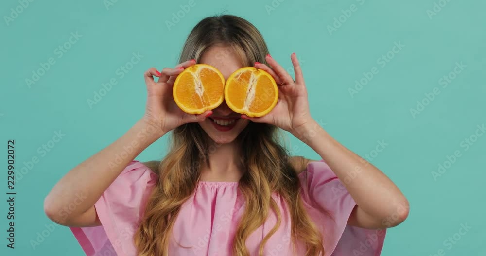 Charming young blonde woman on blue background in studio hold grapefruit poses looks to camera and smiles happy fresh beauty health adult orange skin citrus fashion vitamin vegetarian portrait Charming young blonde woman on blue background in studio hold grapefruit poses looks to camera and smiles happy fresh beauty health adult orange skin citrus fashion vitamin vegetarian portrait