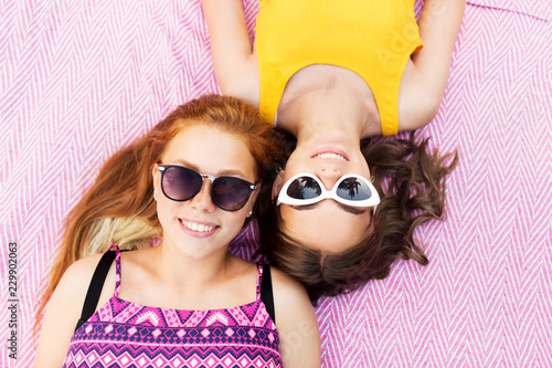 summer fashion, eyewear and people concept - smiling teenage girls in sunglasses lying on picnic blanket
