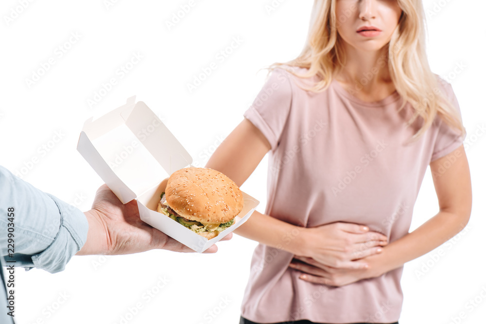 cropped image of blonde woman showing stomach pain, man proposing unhealthy burger isolated on white cropped image of blonde woman showing stomach pain, man proposing unhealthy burger isolated on white