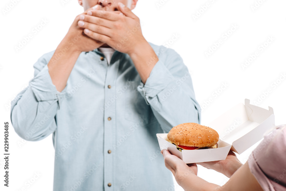 cropped image of man covering mouth, woman proposing burger isolated on white cropped image of man covering mouth, woman proposing burger isolated on white