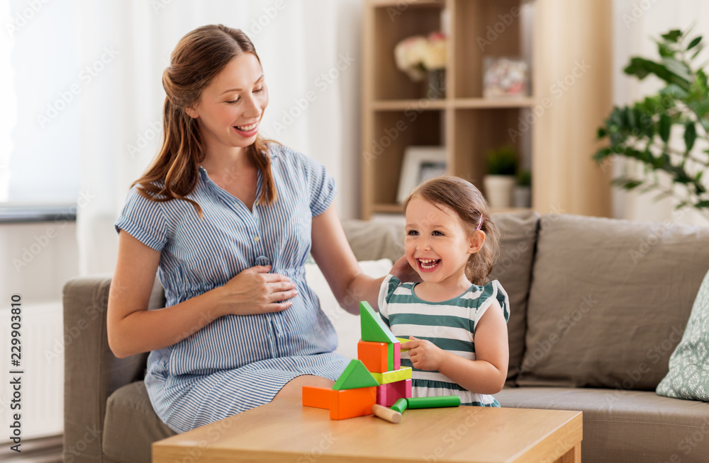 childhood and people concept - happy pregnant mother and little daughter playing with toy blocks at home childhood and people concept - happy pregnant mother and little daughter playing with toy blocks at home
