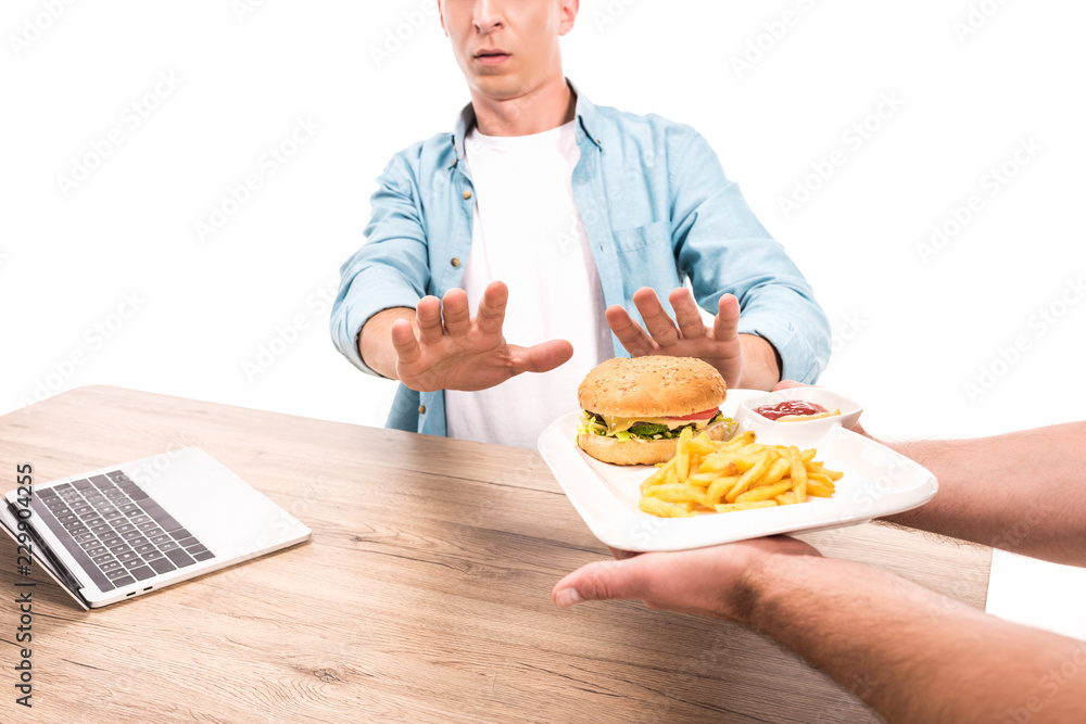 cropped image of man rejecting unhealthy burger and french fries at table isolated on white cropped image of man rejecting unhealthy burger and french fries at table isolated on white