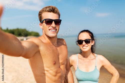 fitness, sport and lifestyle concept - happy couple taking selfie on summer beach