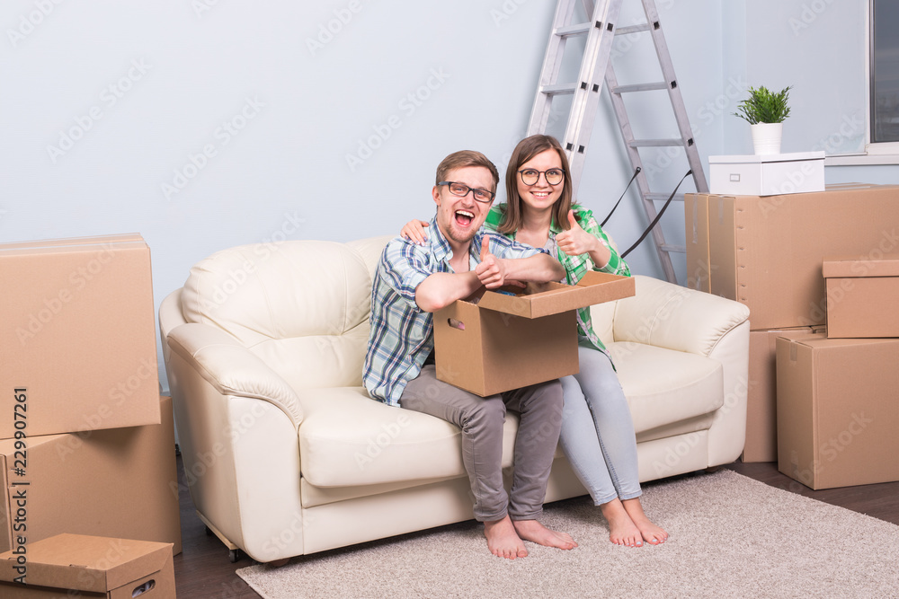 Real estate, relocation and moving concept - happy couple in glasses holding a card board and showing thumbs up Real estate, relocation and moving concept - happy couple in glasses holding a card board and showing thumbs up