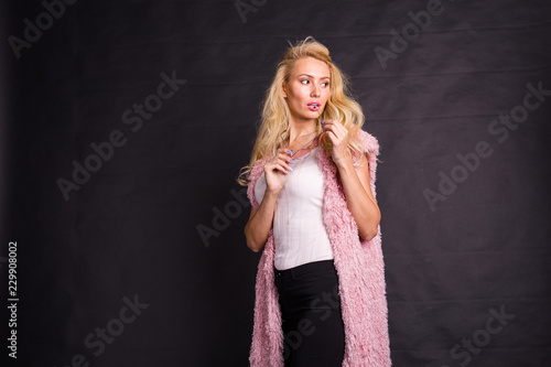 Fashion and beauty concept - portrait of blond model in pink cardigan posing over dark background with copy space © satura_