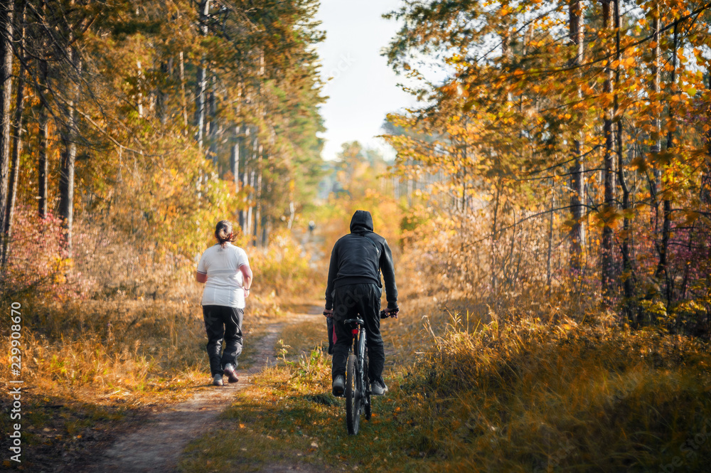 A young woman runs through the woods. The coach is riding a Bicycle nearby. The concept of a healthy lifestyle and weight management