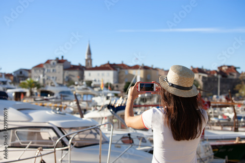 Young travelling woman in hat taking photos of summer sunny sea with smartphone camera. Brunette girl making photography on summer vacation