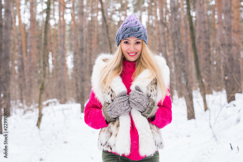 Fashion, winter and people concept - Young attractive woman dressed in fur waistcoat over snowy nature background