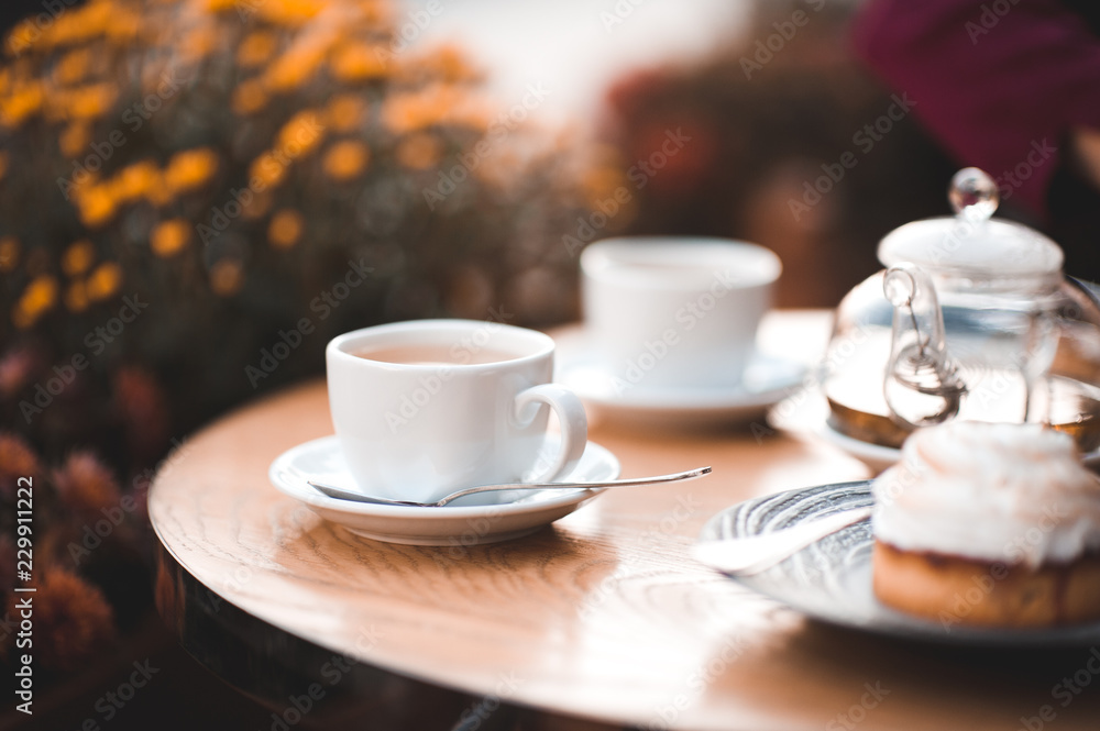 Cup of tea with cake on wooden table in cafe with flowers at background. Good morning. Cup of tea with cake on wooden table in cafe with flowers at background. Good morning.