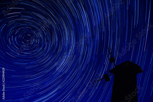 A windmill standing against the sky with a star trail