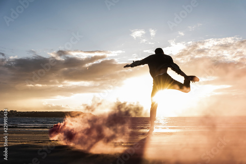 Man doing movement training at the beach with colorful smoke at sunset