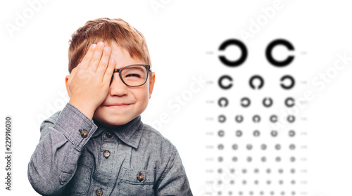 Fototapeta Naklejka Na Ścianę i Meble -  boy having eye exam with eye chart and covering one eye.