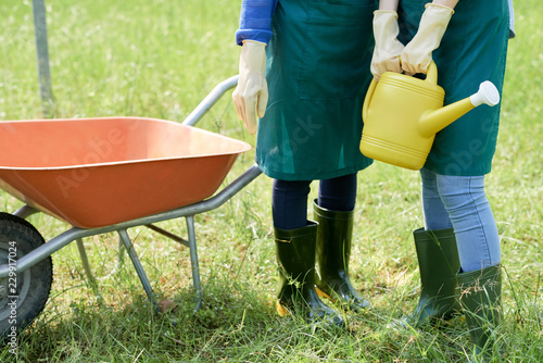 Close-up of two gardeners in uniform and rubber boots standing with trolley and watering can and are ready for work