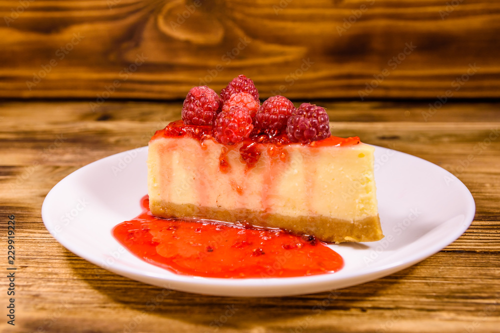 White plate with cheesecake New York and raspberries on wooden table White plate with cheesecake New York and raspberries on wooden table