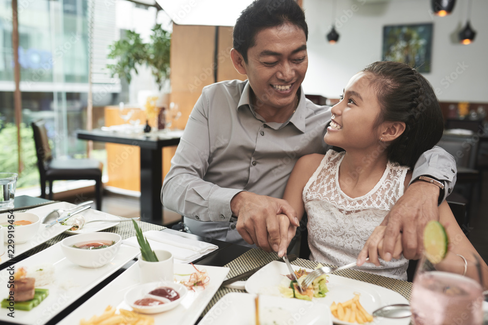 Happy father eating together with his cute smiling daughter at the table at restaurant Happy father eating together with his cute smiling daughter at the table at restaurant