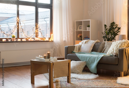 interior, christmas and interior concept - cushioned sofa, coffee table, garland string and candles on window sill in living room of cozy home photo