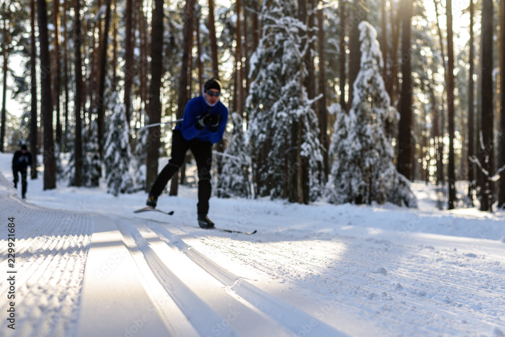 Classic ski track in the forest, in the background in the blur of the skier in winter clothes and glasses to roll down the slope