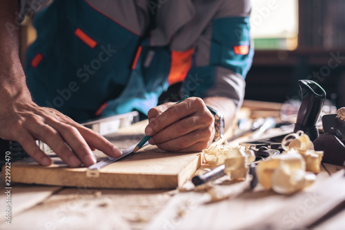 Construction, roofing, woodworking. Close-up of the hands of a carpenter, a worker with a pencil makes a mark on a wooden board