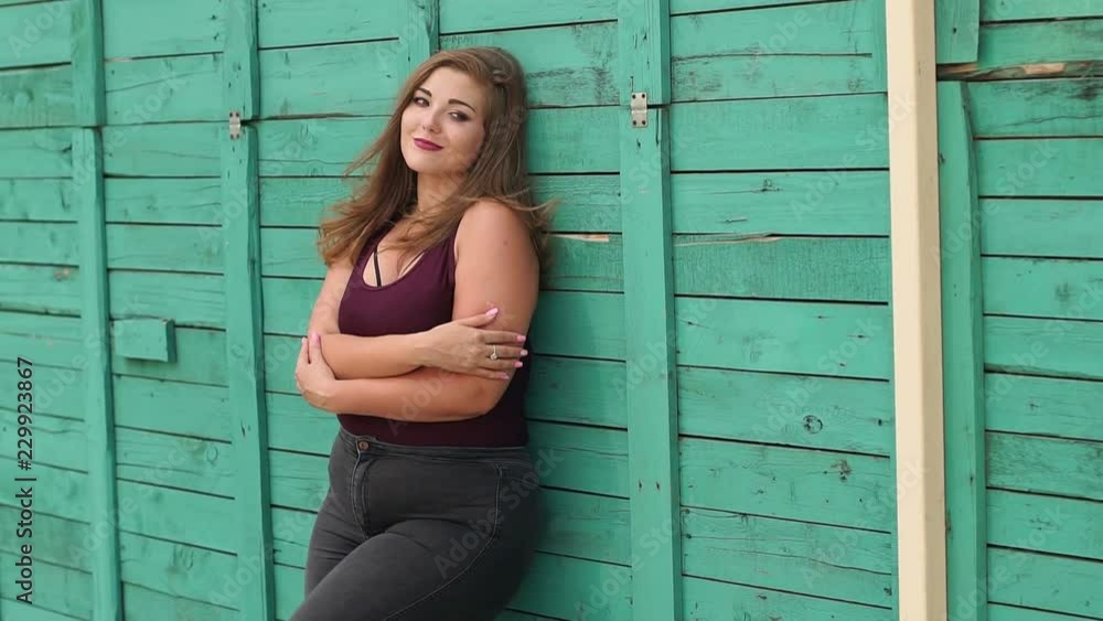 Portrait of a girl model plus size on the background of a green wall. A young girl with a full figure walks in the Park in the summer against a green wooden wall.