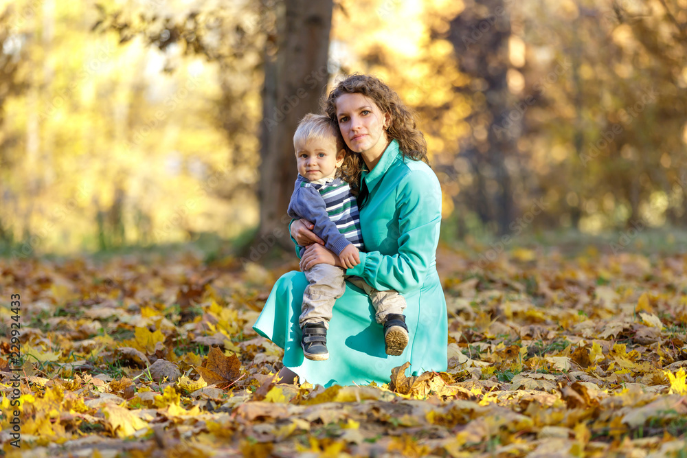 Young mother with little kid sitting on autumn leaves Young mother with little kid sitting on autumn leaves