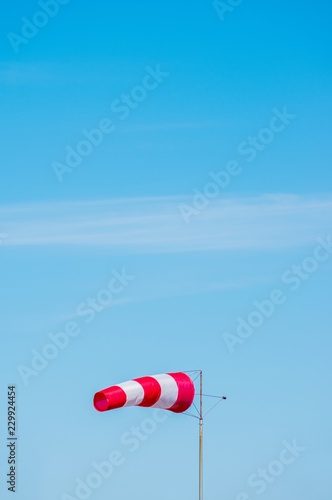 Windsock on blue sky background. Red and white stripe textile in wind with slightly cloudy sky. Indicating direction and speed of wind.