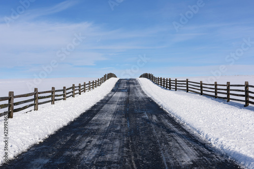 Winter Scene of Road with Fence - looking up small hill with blue skies © junej