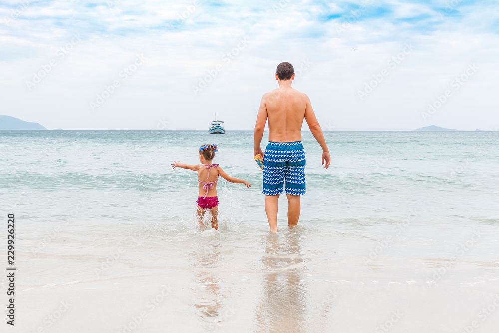 dad and little daughter walk on the beach