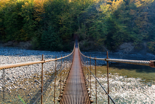 Fototapeta Naklejka Na Ścianę i Meble -  Narrow metal foot bridge across river in autumn