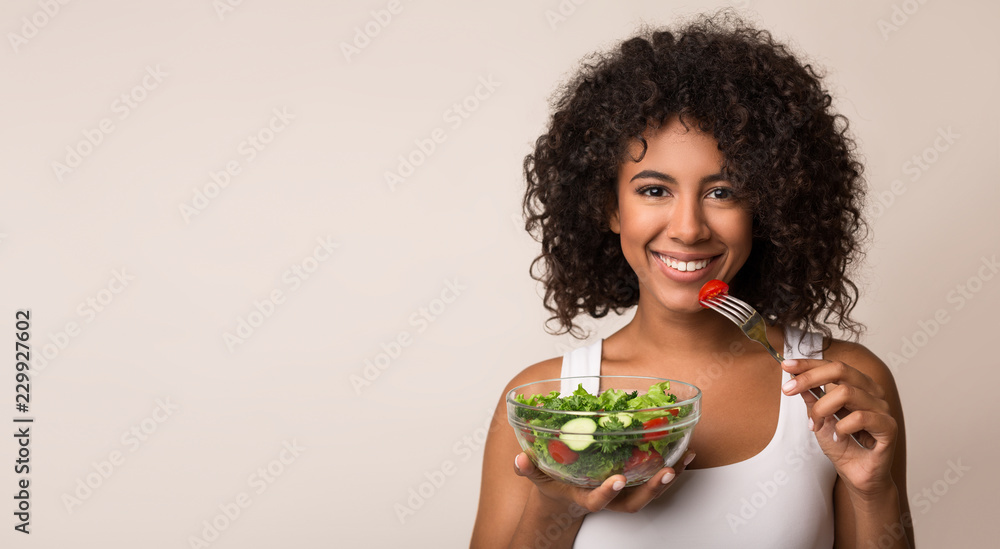 African-american woman eating vegetable salad over light background - obrazy, fototapety, plakaty 