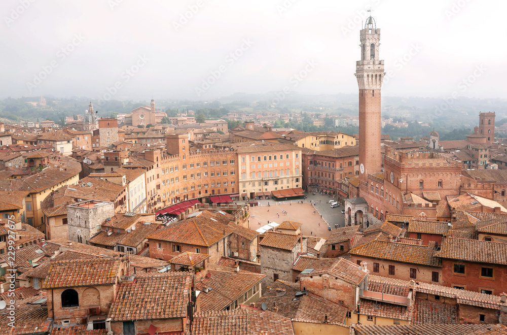 Beautiful old buildings under morning mist in Siena, Tuscany. Tile roofs and 14th century tower Torre del Mangia, Italy. UNESCO World Heritage Site