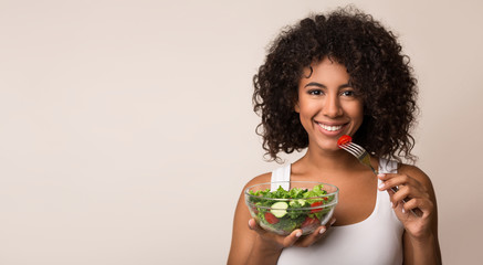 African-american woman eating vegetable salad over light background