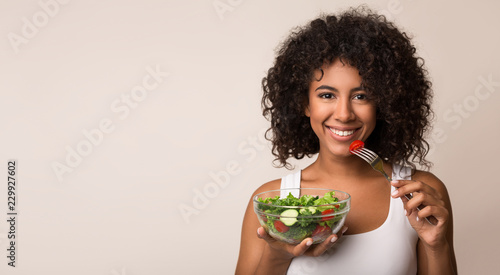 African-american woman eating vegetable salad over light background