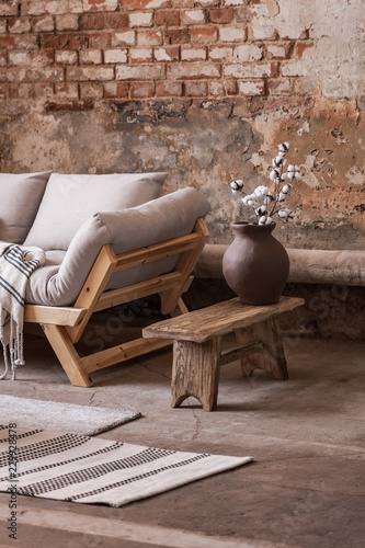 Flowers on wooden stool next to beige sofa in living room interior with red brick wall. Real photo