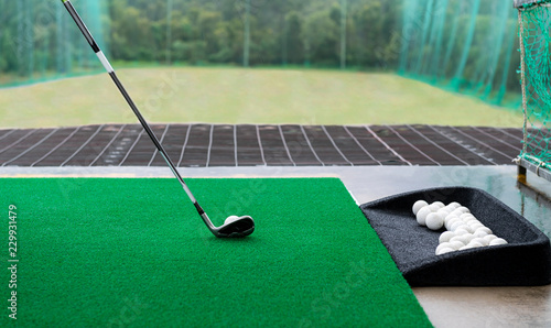 Golf club and ball on a synthetic grass mat at a practice range.