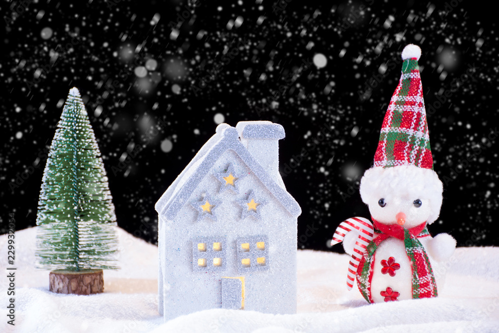 Christmas night idyll with small house toy and snowman and fir tree. It's snowing and snowflakes falling down. Winter and holiday concept image