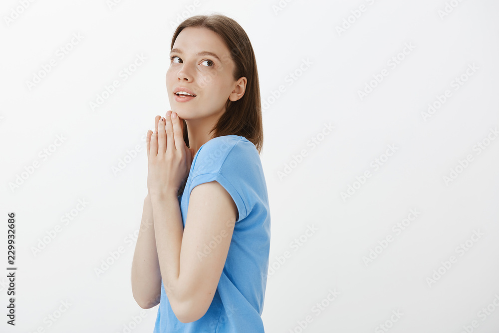 Girl waiting with temptation for important call. Impatient attractive european woman with fair hair, standing in profile with clenched palms above chin and gazing right, awaiting for something Girl waiting with temptation for important call. Impatient attractive european woman with fair hair, standing in profile with clenched palms above chin and gazing right, awaiting for something