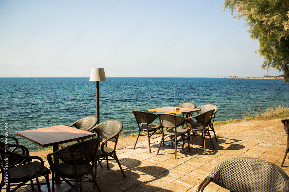 open air patio cafe furniture tables and chairs on shore line of tropic Mediterranean sea in summer hot weather time