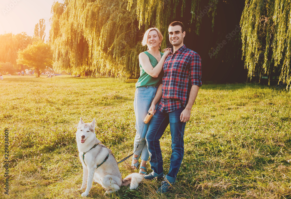 Fototapeta premium Dog with owners spend a day at the park. Young couple and husky running, playing and having fun.