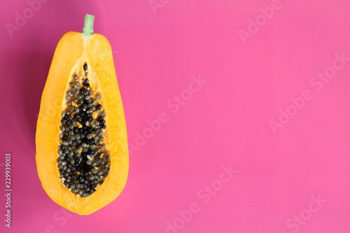 Half of ripe papaya with seeds isolated on pink background