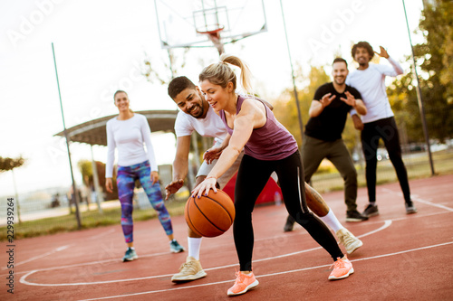 Group of multiracial young people playing basketball outdoors