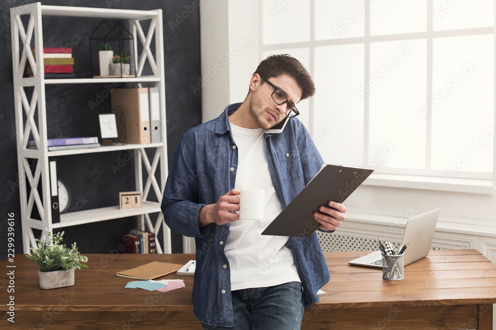 Fototapeta premium Pensive young businessman talking on mobile and reading documents
