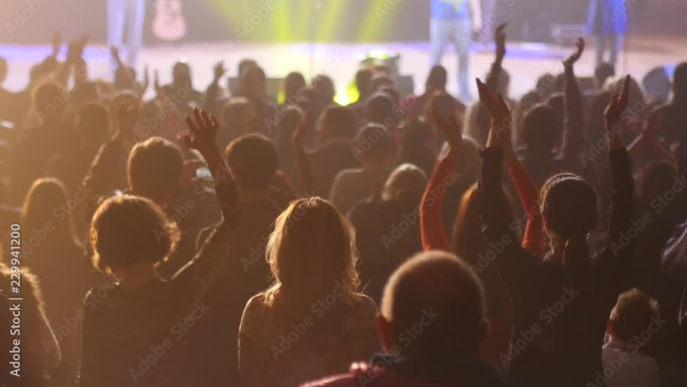 Audience cheerfully applauds clapping hands at the concert flashing spotlights to performer