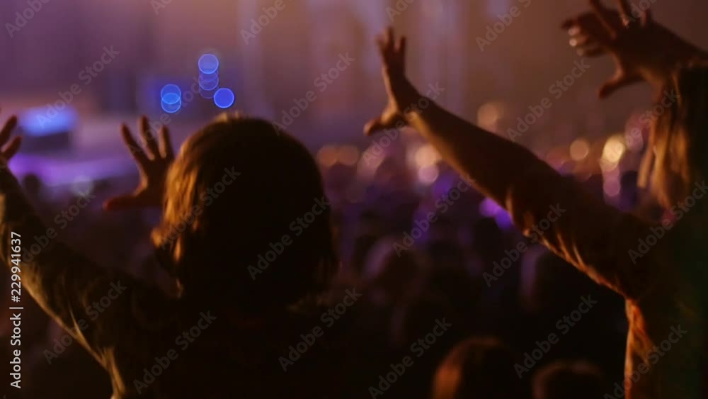Dancing girl fan silhouettes on a concert flashing light cheerful hands in air